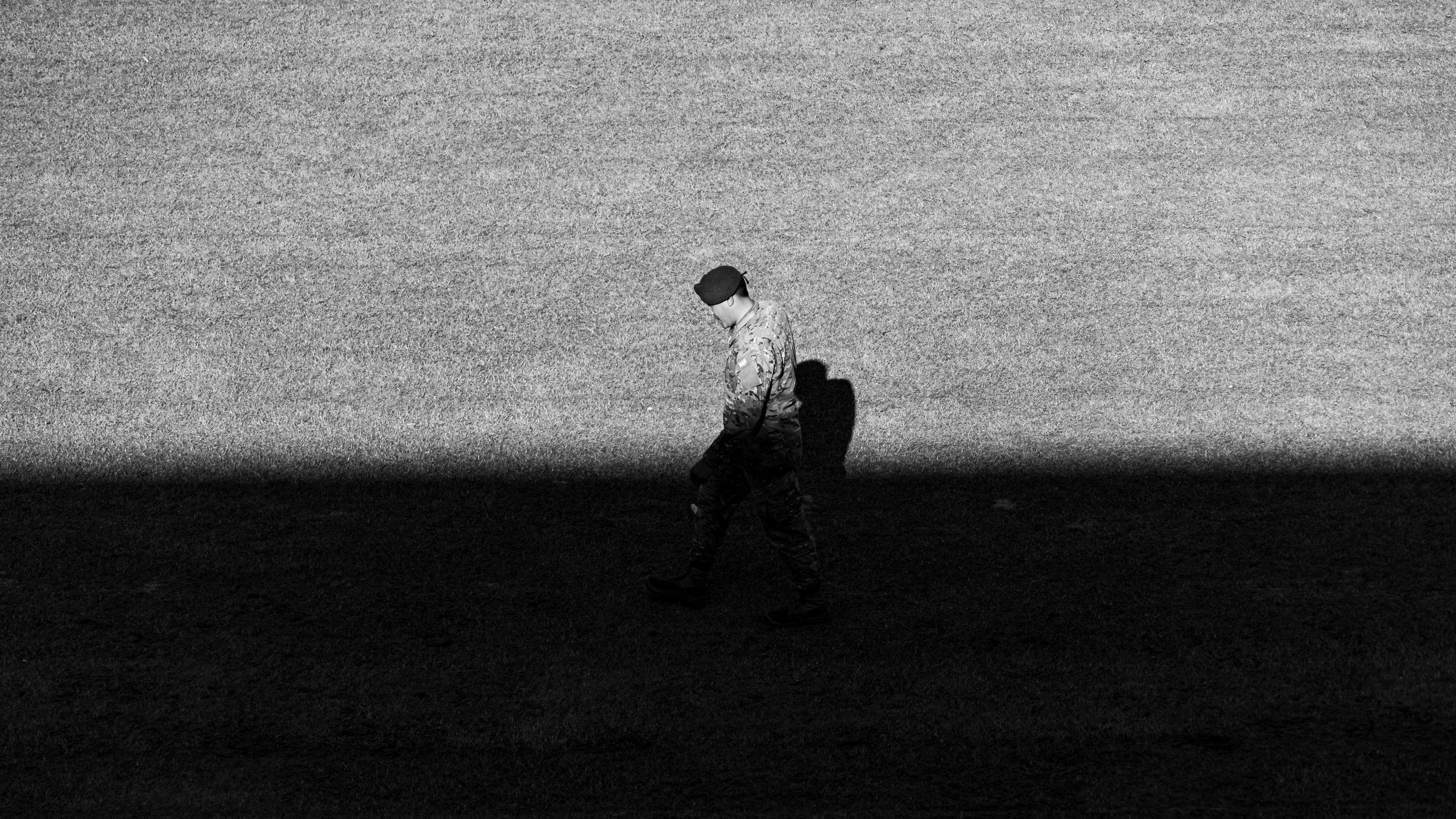 Black and white image of a soldier walking in a shadowed area.